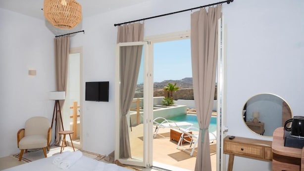 Habitación de hotel con cama, una silla, un escritorio, un espejo y vistas a una piscina y al paisaje.