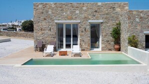 Un edificio moderno de piedra con piscina, mobiliario exterior y vistas al mar.