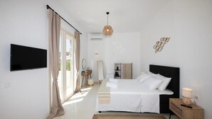 A bedroom with a bed, bedside table, lamp, and a TV mounted on the wall. - Adyton Luxury Suites Mykonos Poolside Luxury (Mykonos)
