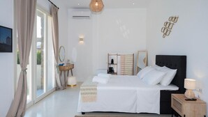 A bedroom with a large bed, bedside tables, a nightstand, a hanging light fixture, and a wall-mounted mirror. - Adyton Luxury Suites Mykonos Poolside Luxury (Mykonos)