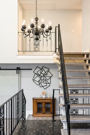Una escalera con barandilla negra, un candelabro y una obra de arte geométrica en la pared.
