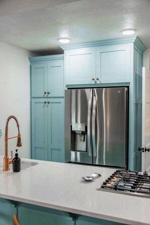 Una cocina con armarios azul claro, un refrigerador de acero inoxidable, dispensador de agua, grifo de cobre y estufa a gas.