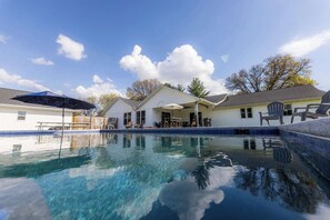 Una piscina con agua cristalina azul, rodeada por un edificio blanco con un patio cubierto.