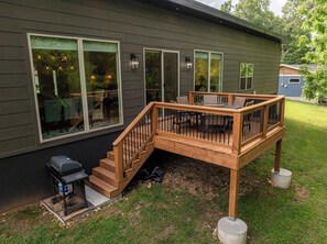 Une maison dotée d’une terrasse, d’un barbecue et d’une grande fenêtre donnant sur un jardin.