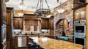 A kitchen with a large island, wooden cabinets, a stone accent wall, and a built-in oven. - The Highlands mansion, sleeps 28 (Decatur)