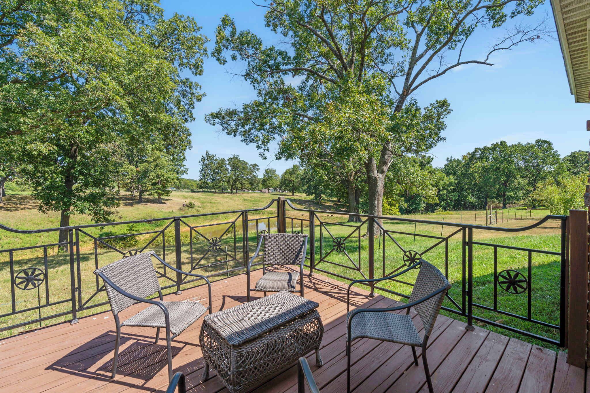A wooden deck with wicker furniture and a view of a grassy field and trees.