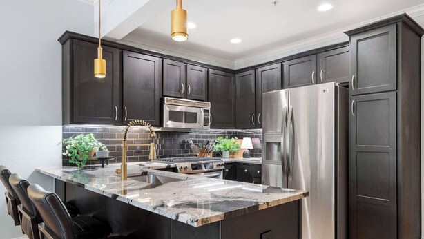 Una cocina moderna con armarios oscuros, electrodomésticos de acero inoxidable, una isla de mármol y taburetes de cuero negro.