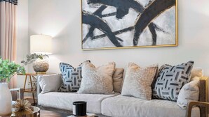 Una sala de estar moderna con un sofá, almohadones decorativos, una mesa de centro, una lámpara y un cuadro abstracto grande en la pared.