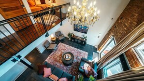 A spacious loft with a high ceiling, a chandelier, a staircase, and a cozy seating area with a coffee table. - The Loft on Campus Su (Fayetteville)