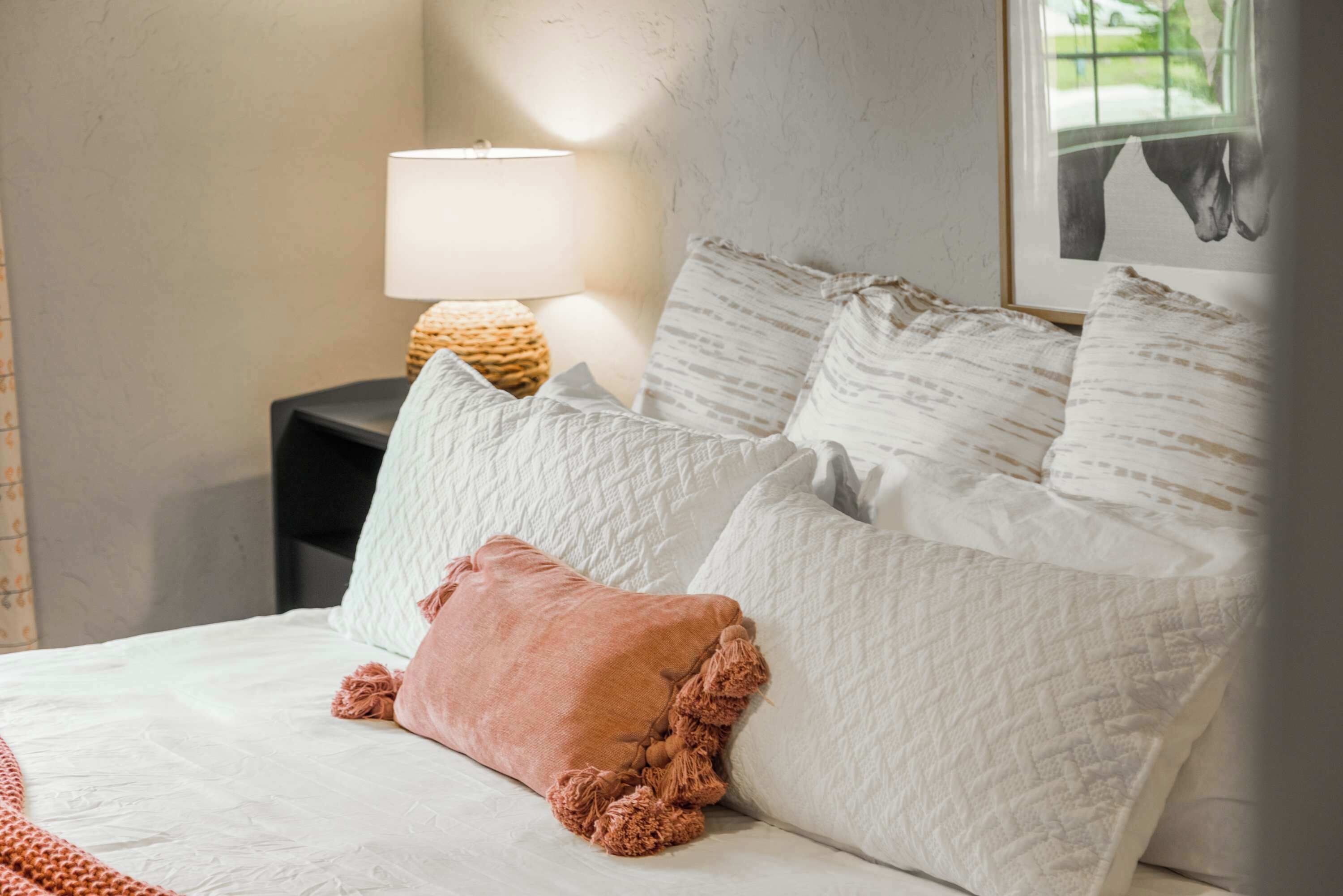 A neatly made bed with white bedding and a single pink pillow.