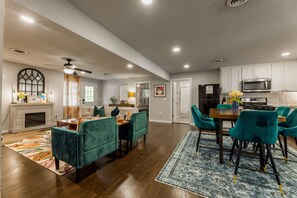 A spacious living room with a fireplace, teal sofas, and a dining area with teal chairs.
