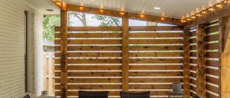 A covered patio area with a wooden fence, a table with chairs, and a ceiling fan.