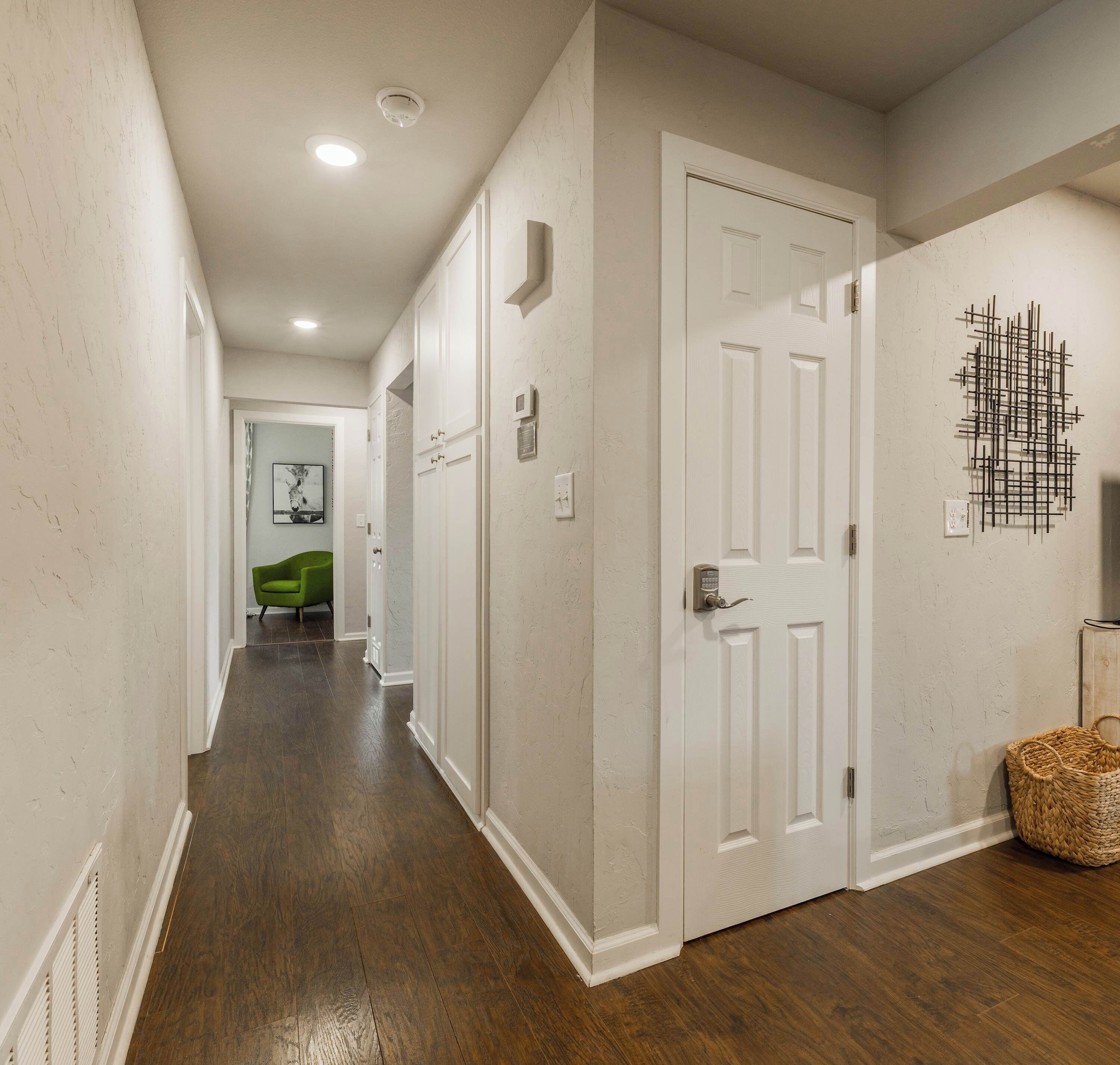 A hallway with wooden flooring, white walls, and a door with a security keypad.