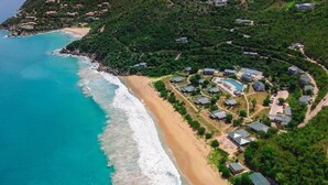 Vista aérea de un resort costero con villas frente a la playa, una piscina y una playa.