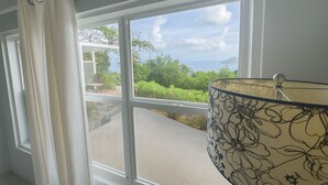 Una habitación con un ventanal grande, vistas a vegetación y un edificio al otro lado de la calle.