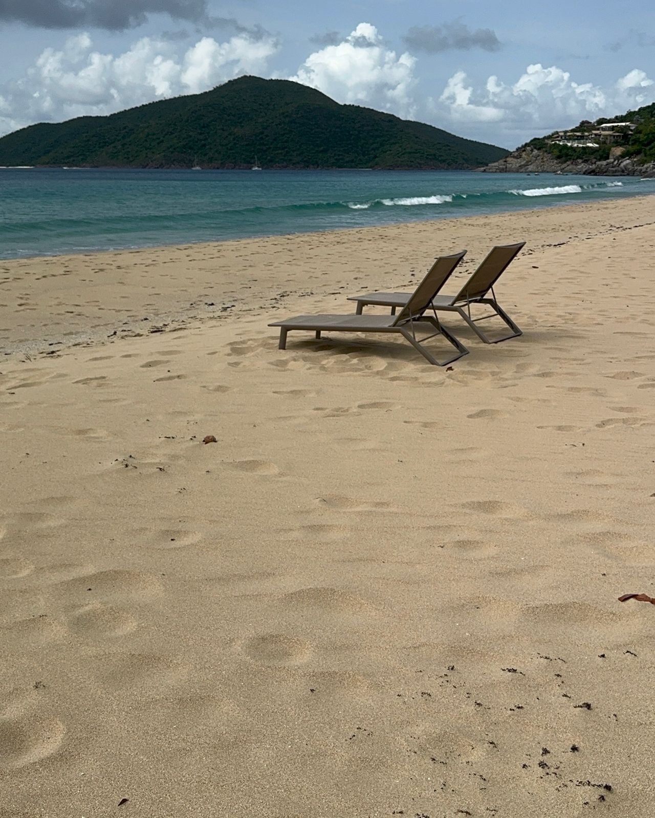A beach with two empty lounge chairs and a mountain in the background.
