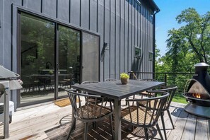 An outdoor deck with a table and chairs, a fire pit, and a sliding glass door leading to an interior space. - Sapphire Lodge at Bella Vista (Bella Vista)