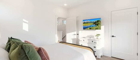 A bedroom with a bed, a dresser, a TV, and a door.