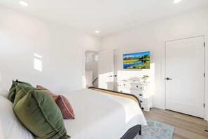 A bedroom with a bed, a dresser, a TV, and a door.