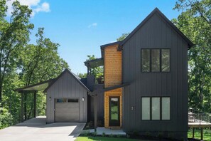 Een modern huis met twee verdiepingen, een garage, een overdekte veranda en een verzorgd gazon.