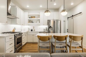 A modern kitchen with white cabinetry, a stainless steel refrigerator, a gas stove, and a dining area with wooden chairs.