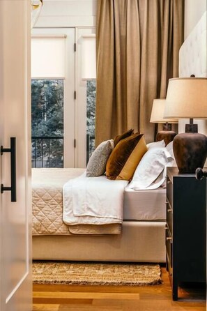 A bedroom with a bed, a nightstand, a lamp, and a view of trees through the window.
