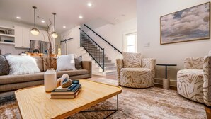 Una sala de estar moderna con un sofá, dos sillones estampados, una mesita de centro y una escalera.