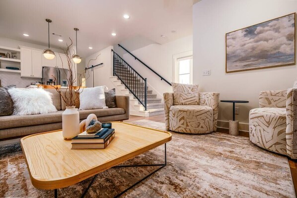 A modern living room with a sofa, two patterned armchairs, a coffee table, and a staircase.
