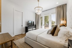A bedroom with a bed, a TV, a lamp, and a view of the outdoors.