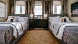 Habitación doble con dos camas, una mesita de noche con lámparas, un libro titulado “The Travel Book” y una ventana con cortinas.