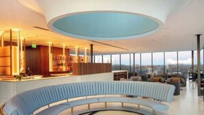 Un espacio lounge moderno con una disposición curva de asientos, un bar y ventanas amplias que ofrecen vistas a la ciudad.