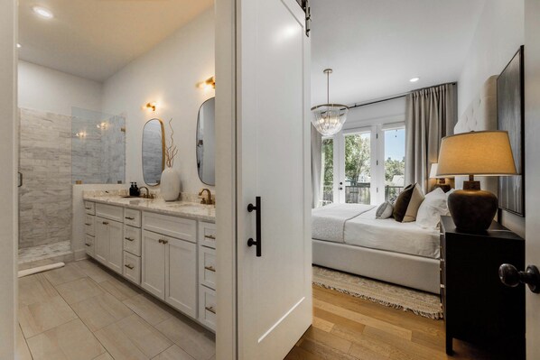 A modern bedroom with a large bed, a bedside table with a lamp, and a view of the outdoors through the window.