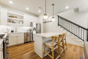 A modern kitchen with white cabinetry, stainless steel appliances, a central island with seating, and a staircase with a black railing.