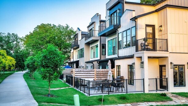 Una hilera de edificios residenciales modernos de varios pisos con balcones, un sendero pavimentado y un pequeño árbol.