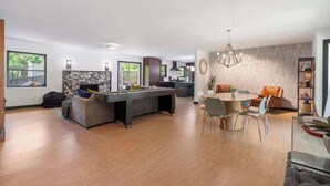 A modern living room with a pool table, dining area, and a kitchen in the background.