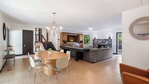 A modern living room with a dining area, a pool table, and a grey sofa.