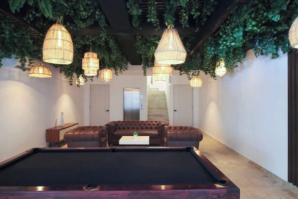 A pool table with a brown leather sofa and a coffee table in a room with hanging lights and green foliage. - Tulum Condo w/ Rooftop, Pool, Gym, Cowork, Cinema (Tulum)