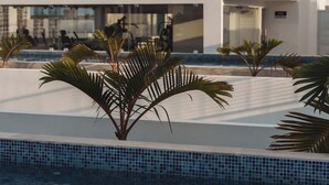 A modern building with a pool area, palm trees, and a clear sky. - Rooftop Pool + Gym + Laundry + Coworking + Cinema (Tulum)