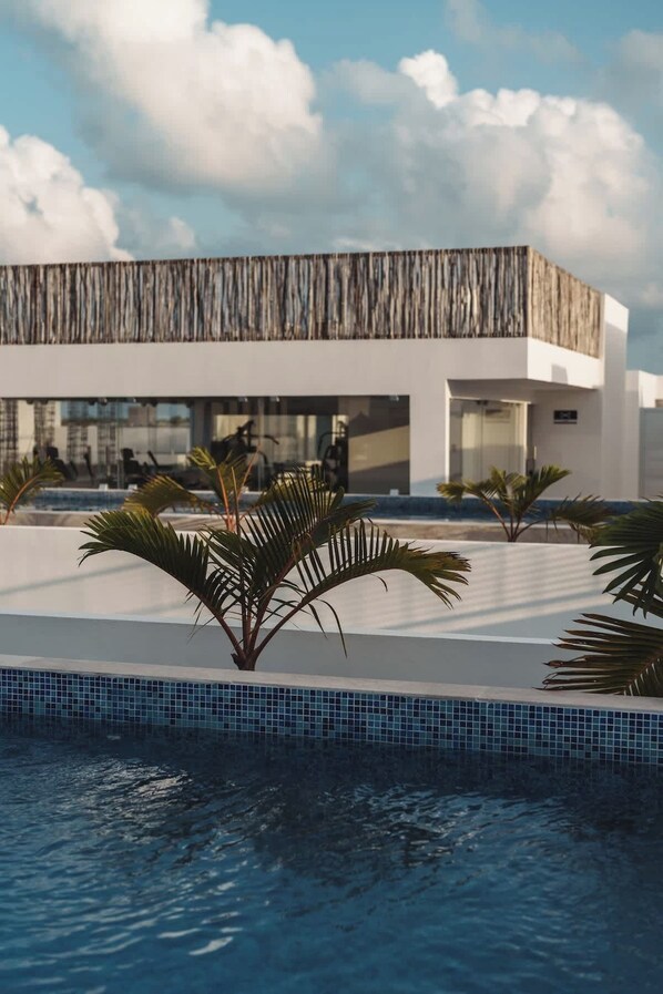 A modern building with a pool area, palm trees, and a clear sky. - Tulum Condo w/ Rooftop, Pool, Gym, Cowork, Cinema (Tulum)