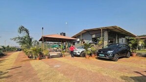 A paved area with a covered seating area, two cars parked, and potted plants.