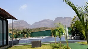 A view of a pool area with a green fence, palm trees, and mountains in the background.