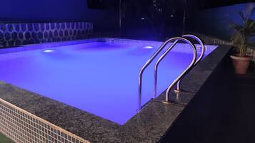 Una piscina con un borde iluminado en azul, una escalera metálica y una planta en maceta.