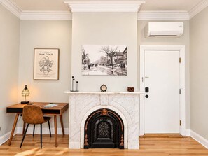 A room with a fireplace, a desk with a chair, a framed artwork, and a door. - Jennifer's Spa-Like Apt King Bed Historic Broadway (Providence)