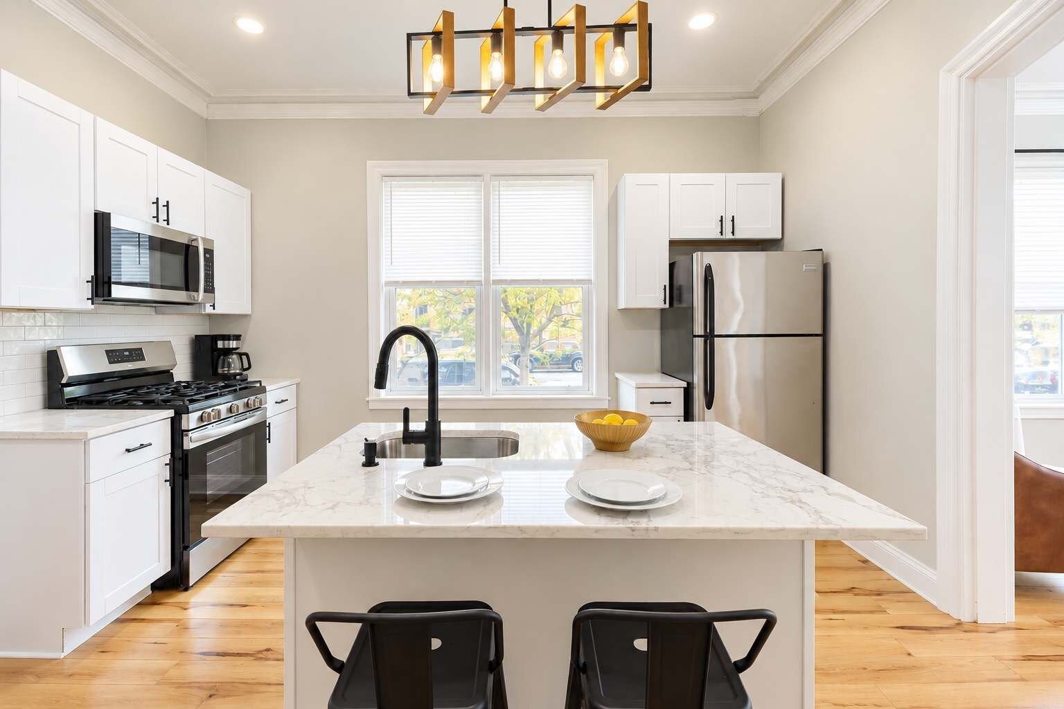A modern kitchen with white cabinetry, stainless steel appliances, a marble countertop, and a black faucet.