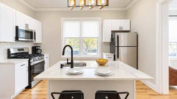 A modern kitchen with white cabinetry, stainless steel appliances, a marble countertop, and a black faucet.