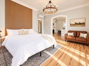 A bedroom with a large bed, a wooden slat wall, a chandelier, and a view into the adjacent living area. - Jennifer's Spa-Like Apt King Bed Historic Broadway (Providence)