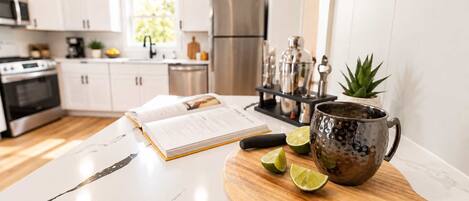 Una cocina moderna con armarios blancos, un refrigerador de acero inoxidable, una tabla de cortar de madera con medio limones y una taza decorativa.