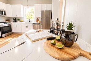 Eine moderne Küche mit weißen Schränken, einem Edelstahlkühlschrank, einem Holzer Schneidebrett mit Limettenhälften und einer dekorativen Tasse.
