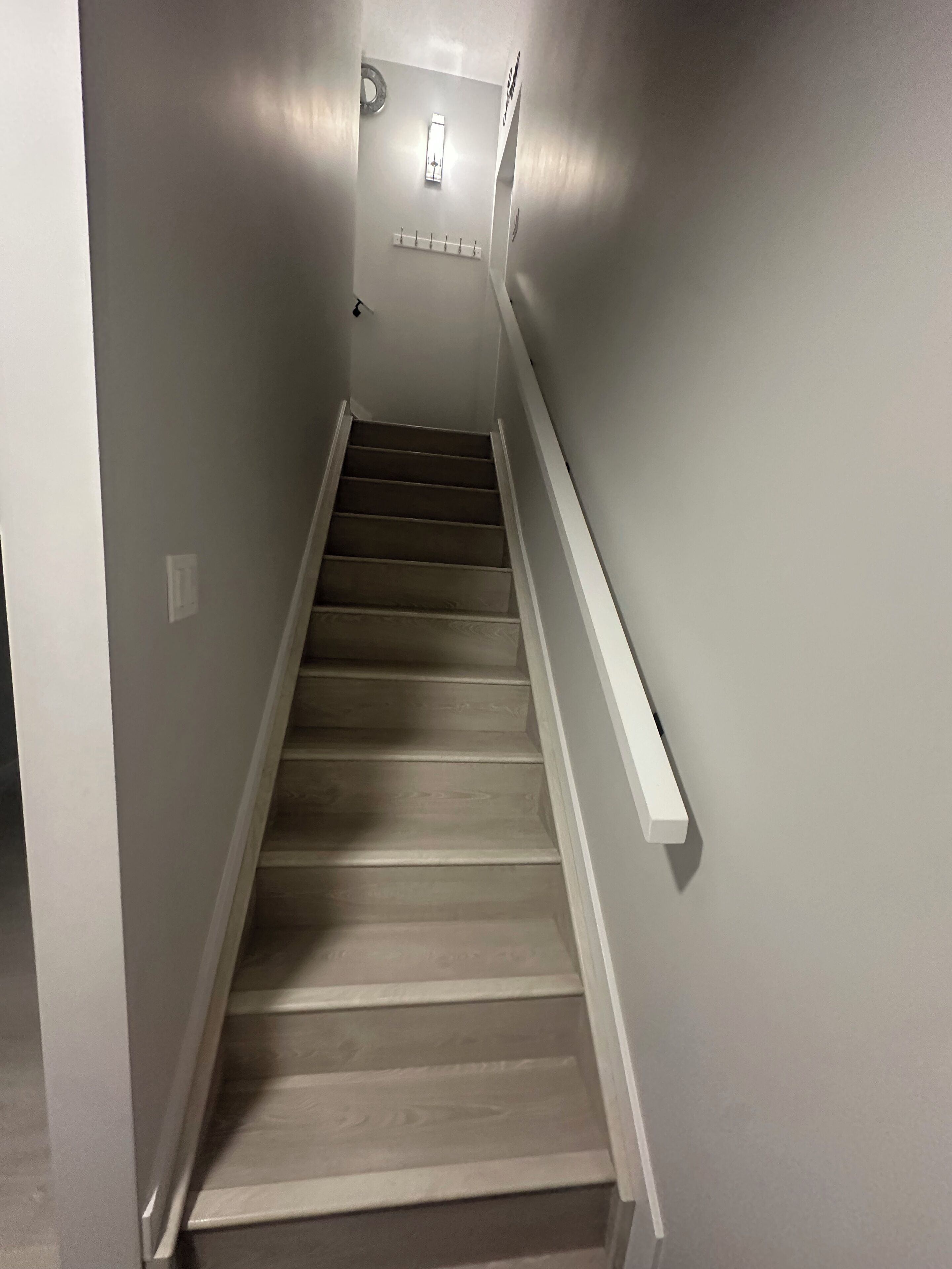 Un escalier étroit, doté d’une main courante d’un côté et d’un luminaire fixé au mur en haut.