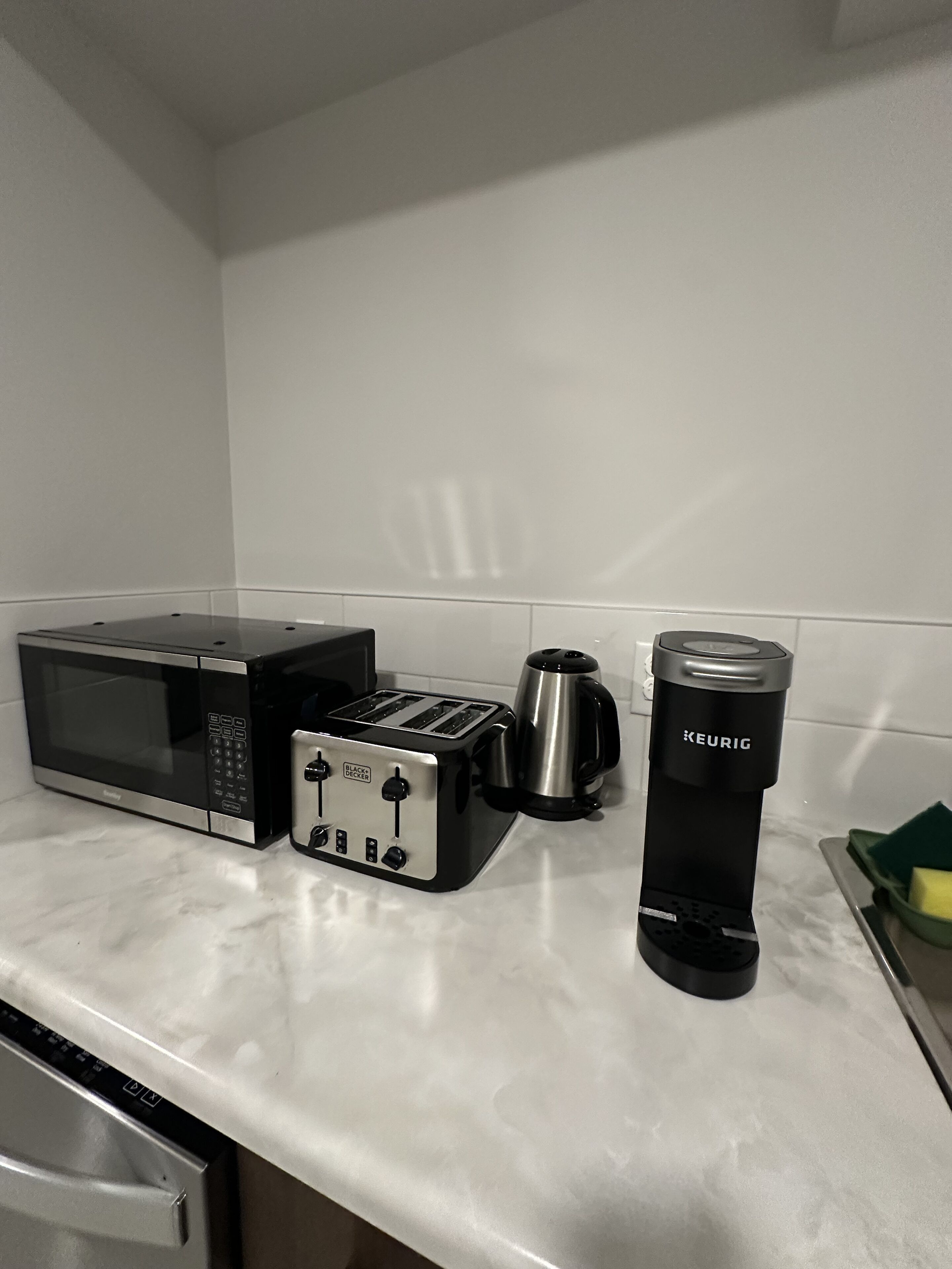 A kitchen with a microwave, toaster, coffee maker, and a kettle on a marble countertop.